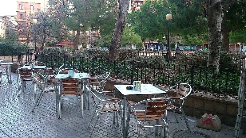 La terraza de Bon Paladar en la plaza de Raquel Payà: las mesas y las sillas de aluminio sobre la acera, la valla del jardín detrás y el parque al otro lado.
