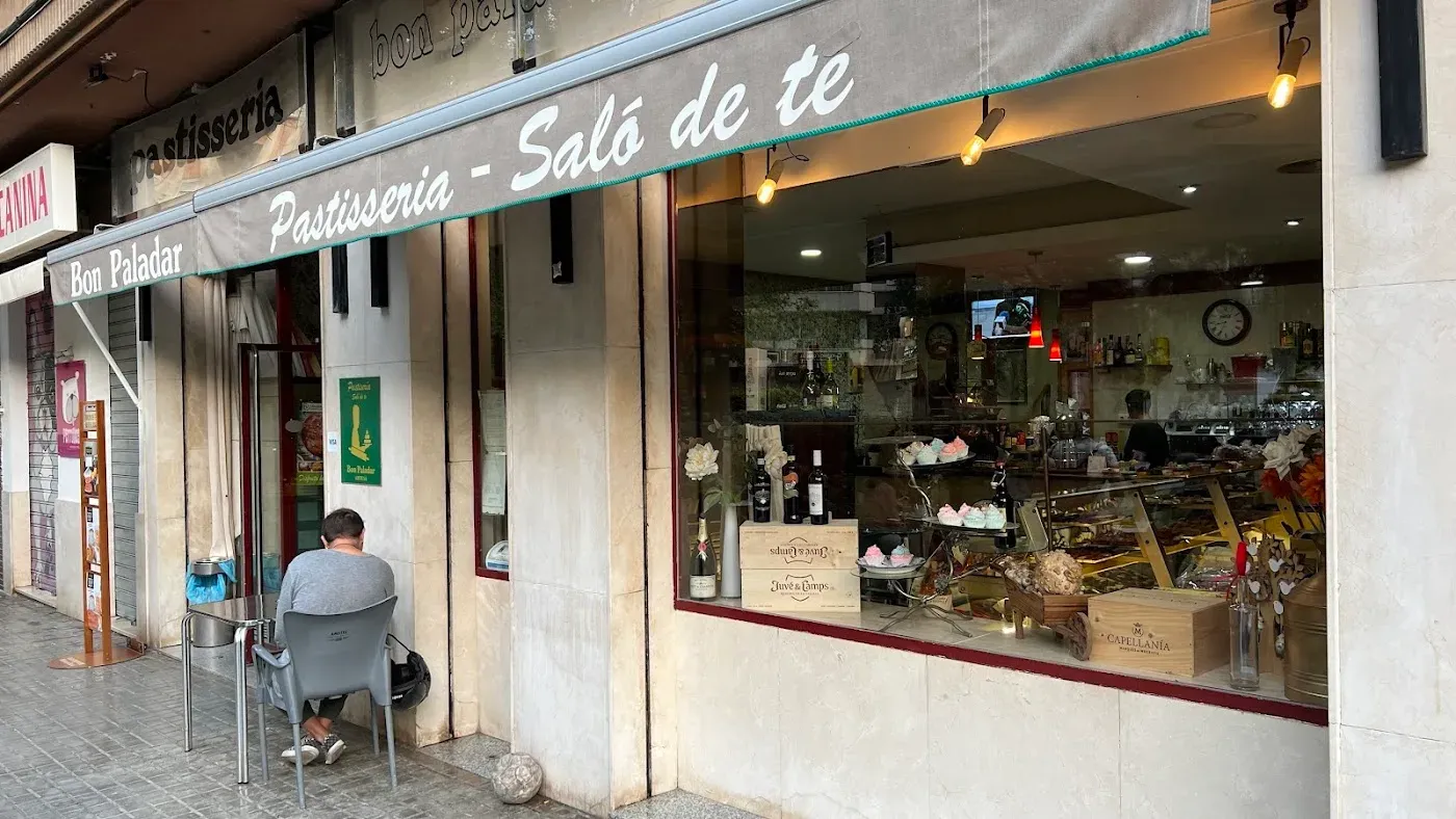 Escaparate de Bon Paladar visto desde la calle, con las bandejas de pastelería iluminadas y el toldo del salón de té encima.